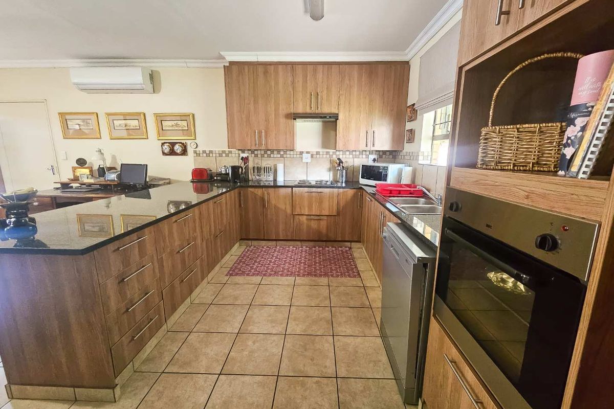A functional U-shaped kitchen featuring wood-look cabinetry, dark granite countertops, tiled flooring, and built-in oven with extractor fan.