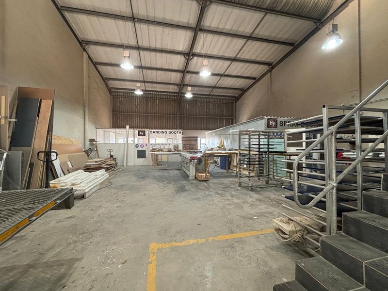 Spacious industrial workshop area featuring high ceilings with exposed steel trusses, concrete flooring, and dedicated sanding and spray booth enclosures.