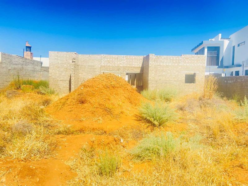 A view of a residential property currently under construction, featuring unrendered masonry walls and an undeveloped garden area.