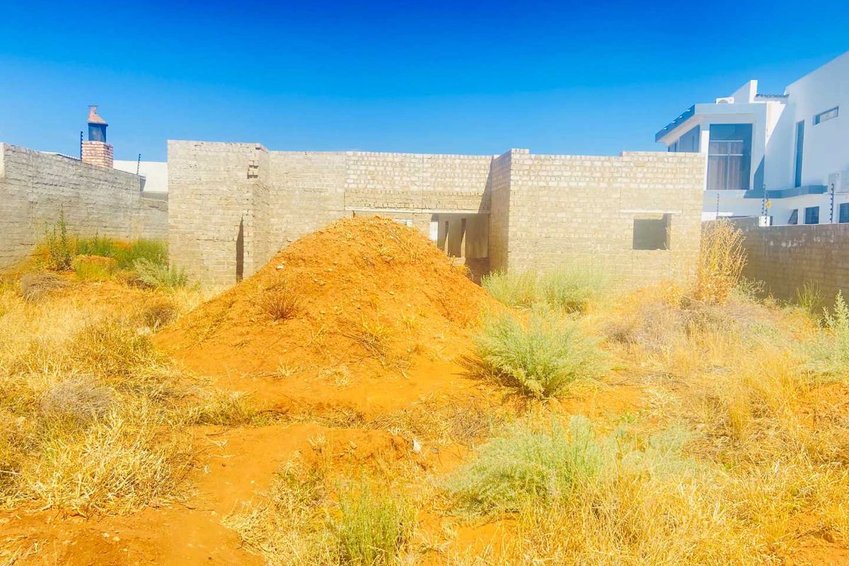 A view of a residential property currently under construction, featuring unrendered masonry walls and an undeveloped garden area.