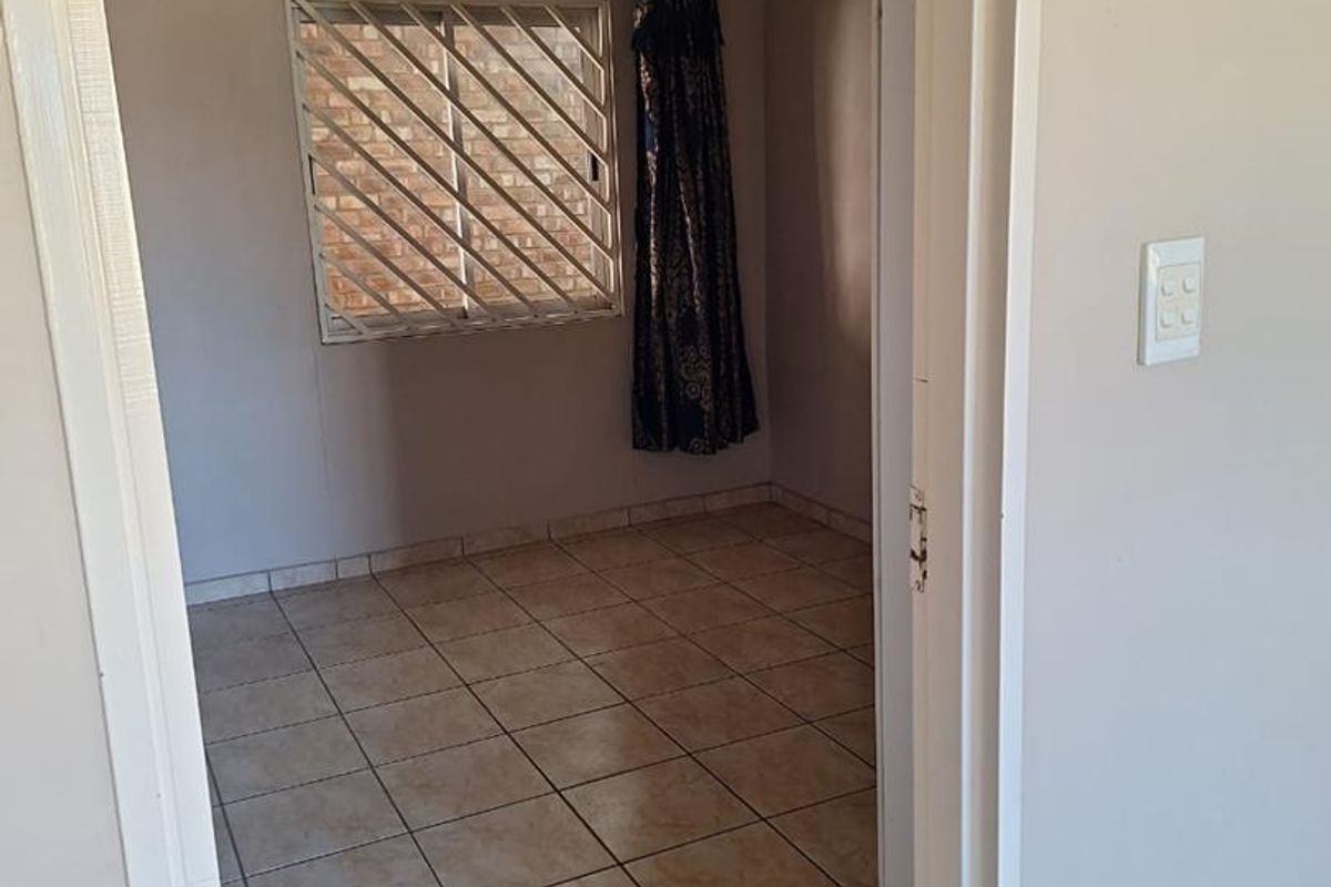 A vacant bedroom featuring tiled flooring, a window with security bars, and a neutral color palette, ready for renovation or staging.