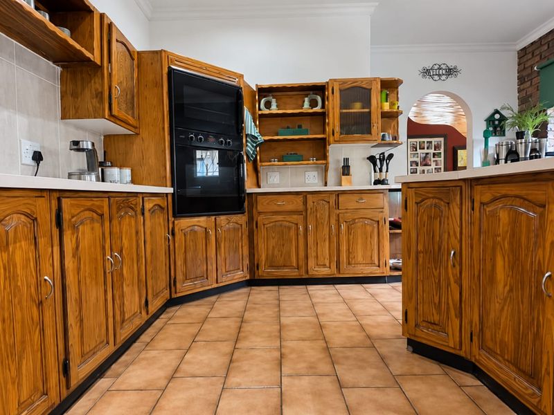 A traditional kitchen featuring extensive wooden cabinetry, built-in oven, tiled flooring, and a distinctive brick wall accent with an arched doorway.