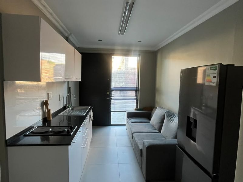 Compact open-plan kitchen and living area featuring modern white cabinetry, granite countertops, tiled flooring, and direct access to an outdoor space.