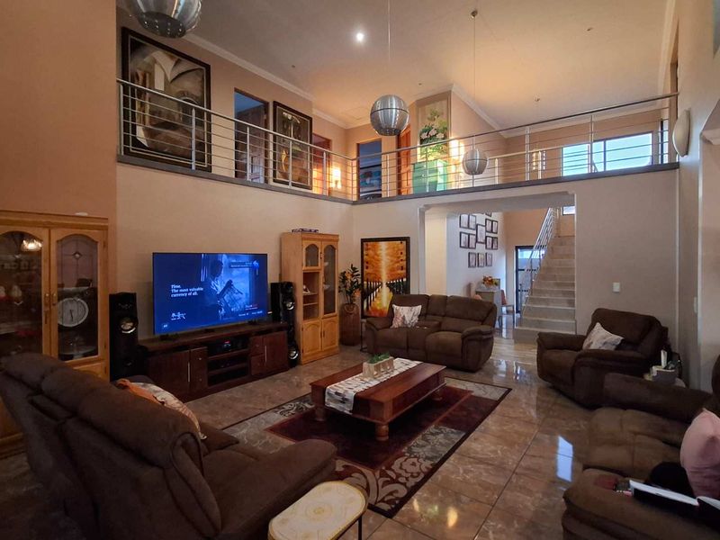 Spacious double-volume living room featuring tiled flooring, a mezzanine level with a stainless steel balustrade, and an open-plan staircase.