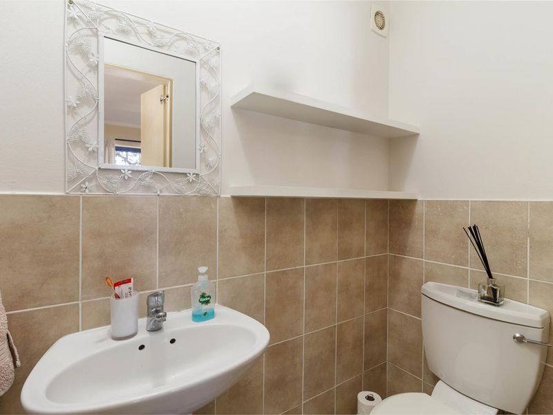 A functional bathroom featuring a pedestal basin, toilet, and wall-mounted shelving with neutral tiled splashbacks.