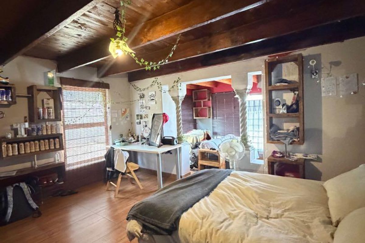 Spacious bedroom featuring exposed timber ceiling beams, warm timber flooring, and unique decorative columns, offering a rustic and character-filled living space.