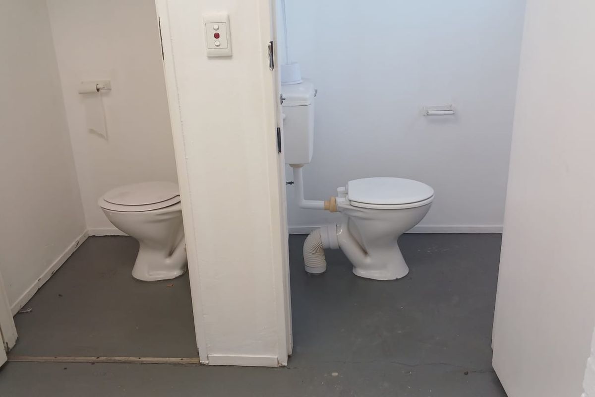 A functional bathroom space featuring two toilets with exposed plumbing and basic fixtures, requiring cosmetic updates to improve the overall finish.