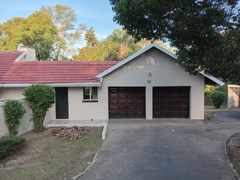 Front elevation of a single-story house featuring a double garage, tiled roof, and a paved driveway with established garden surroundings.