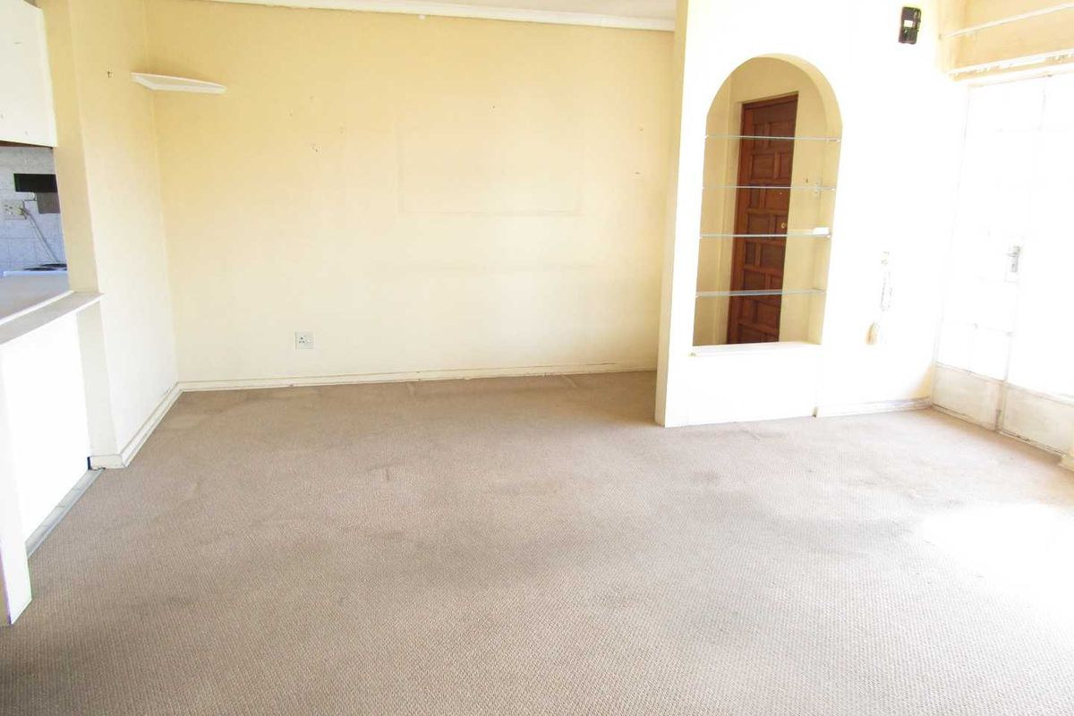 An empty living room featuring a decorative archway with built-in shelving, carpeted flooring, and neutral wall finishes.