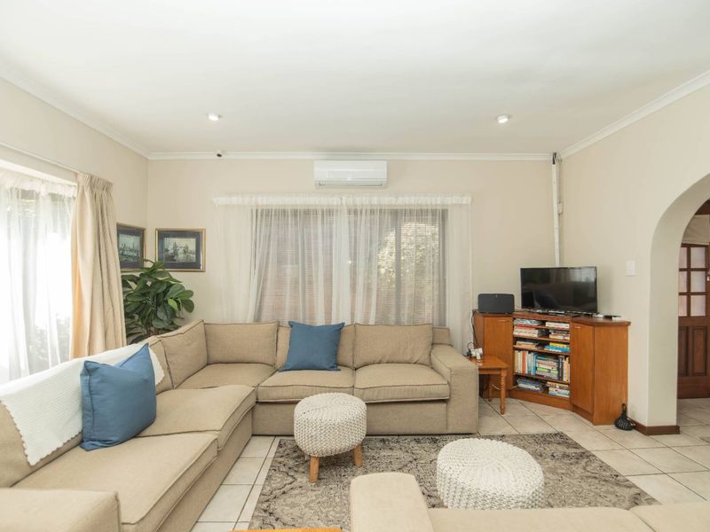 A comfortable living room featuring tiled flooring, recessed downlights, and a wall-mounted air conditioning unit, with an arched entryway leading to adjacent spaces.