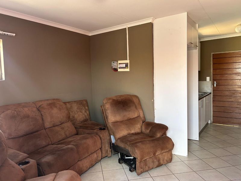 Open plan living area featuring tiled flooring, an exposed electrical distribution board, and a compact kitchen area with built-in cabinetry.