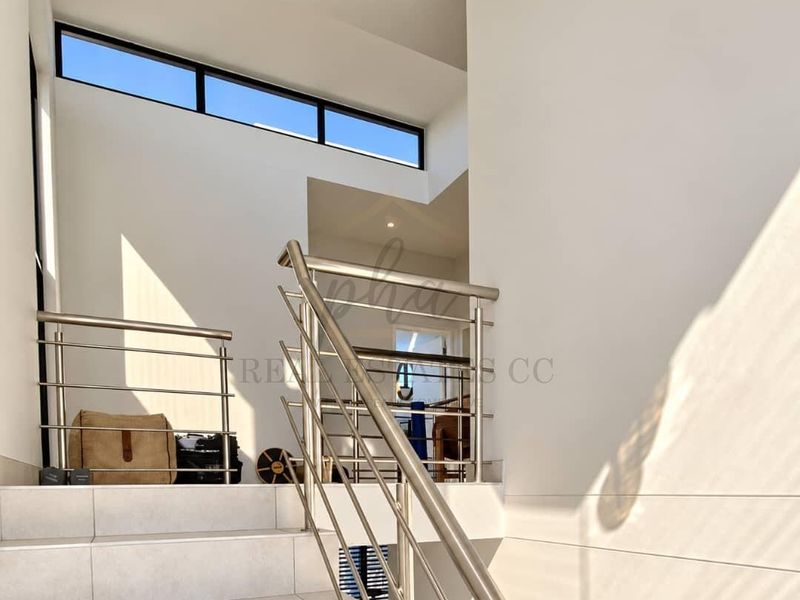 Modern staircase area featuring tiled steps, stainless steel balustrades, and high-level clerestory windows providing natural light.