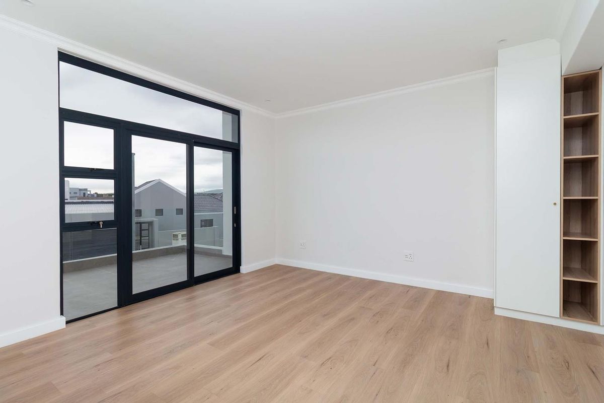A bright, modern bedroom featuring light laminate flooring, built-in shelving, and a large sliding glass door leading to an outdoor balcony.