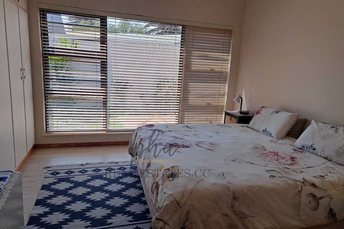 A bedroom featuring built-in cupboards and large windows with fitted blinds, providing natural light and a view of the exterior.