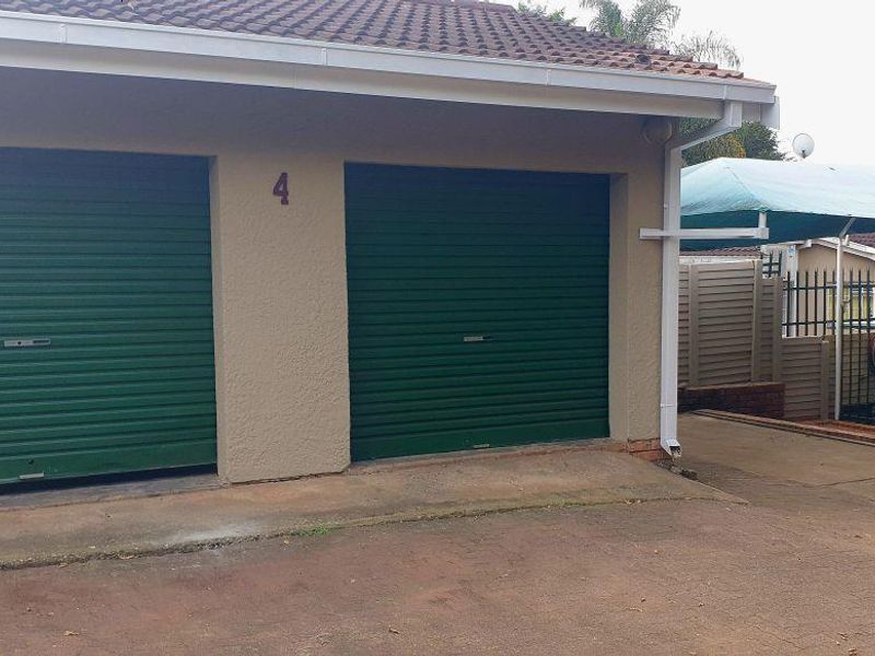 Exterior view of a double garage with green roller doors, featuring a paved driveway and an adjacent carport structure.
