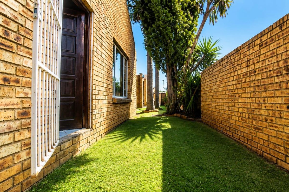 A side garden pathway featuring face brick exterior walls, a secure entrance door, and a well-maintained lawn area enclosed by a boundary wall.