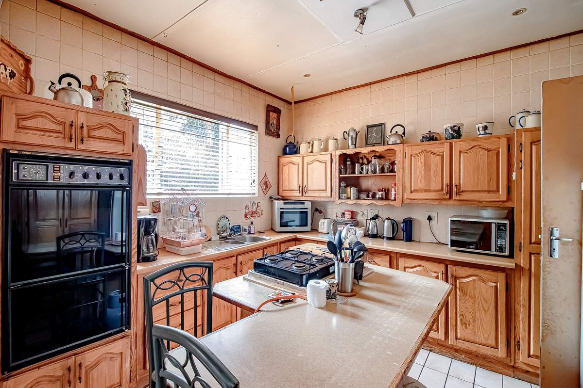 A dated kitchen featuring wooden cabinetry, tiled walls, a built-in oven, and a central island with a gas hob.