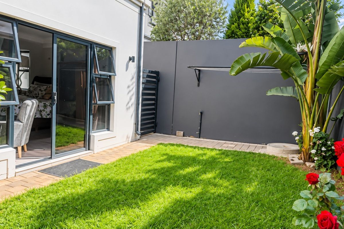 A well-maintained rear garden featuring a paved walkway, manicured lawn, and sliding glass doors providing seamless access to the interior living space.