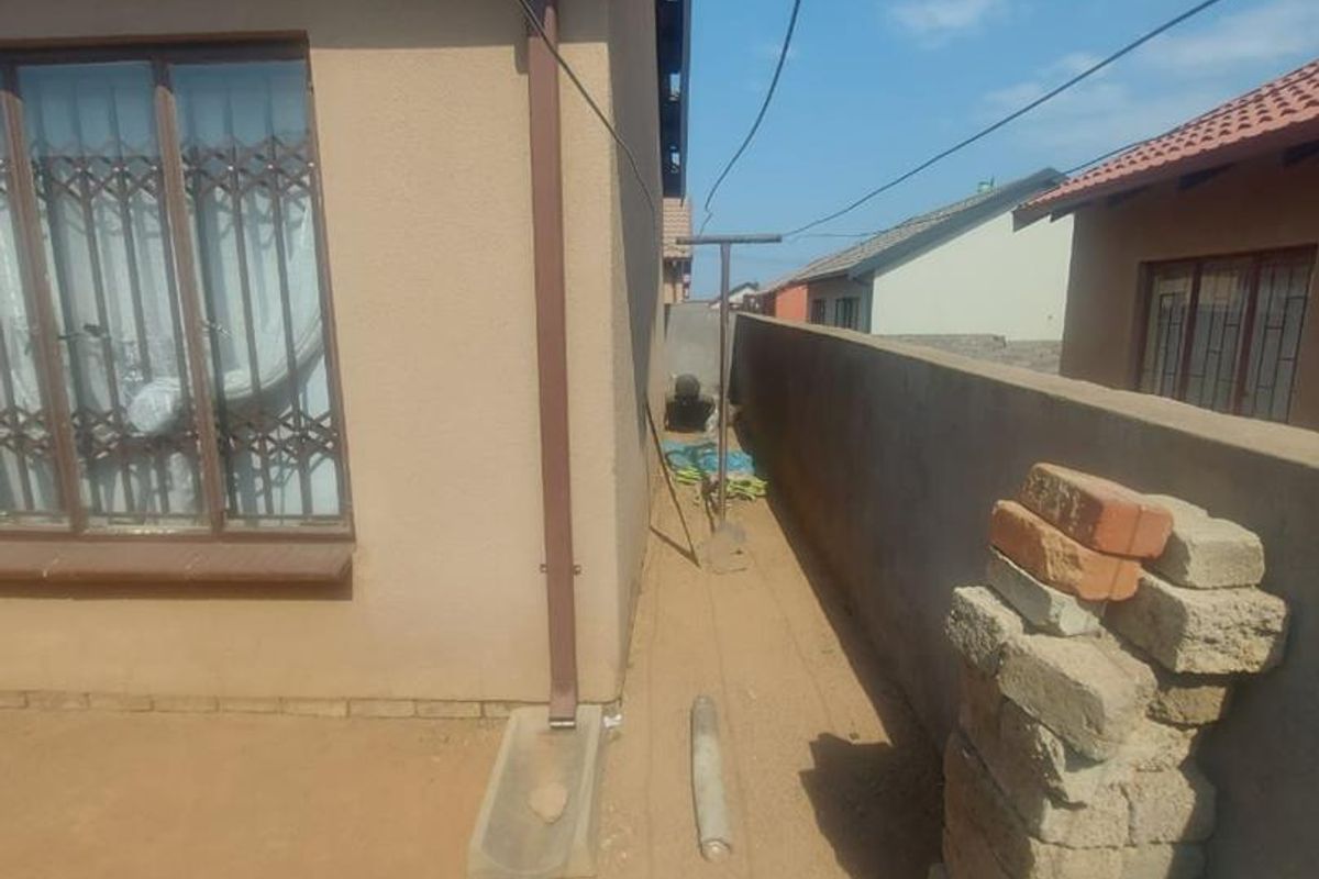 Side exterior view of the property featuring a narrow walkway, perimeter boundary wall, and basic drainage infrastructure.