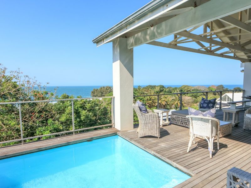 An elevated outdoor pool area featuring timber decking, a covered patio with exposed trusses, and panoramic ocean views.
