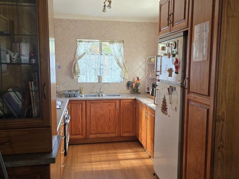 A functional kitchen featuring traditional wooden cabinetry, laminate countertops, a double basin sink, and tiled backsplash, offering a classic, dated aesthetic.