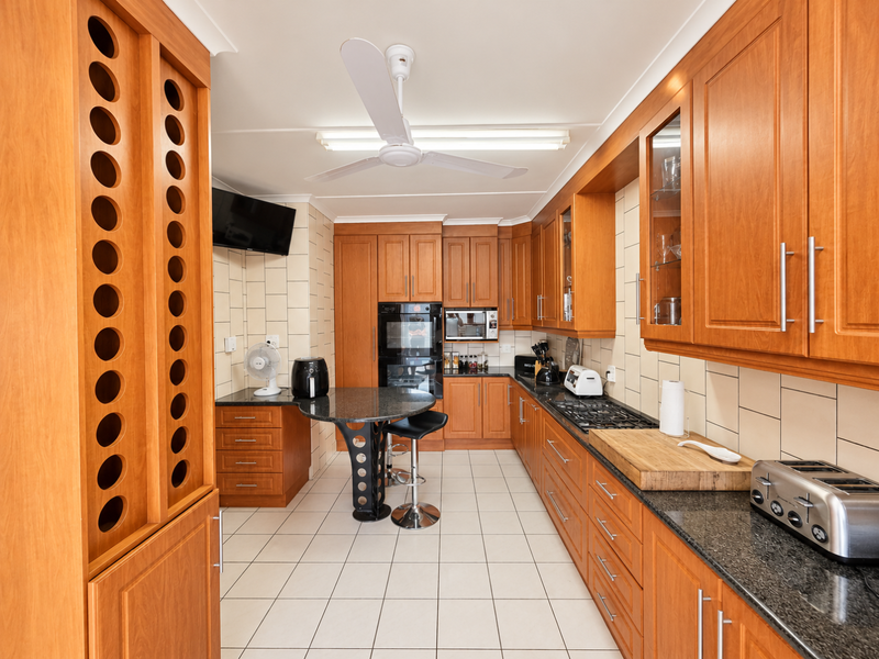 A functional kitchen featuring extensive wooden cabinetry, granite countertops, built-in appliances, and a central breakfast nook with tiled flooring throughout.