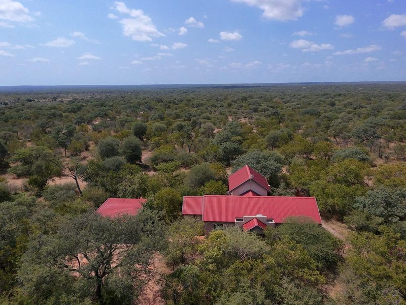 Aerial view of a guest house property featuring red corrugated metal roofing, situated within a vast, natural bushveld landscape.