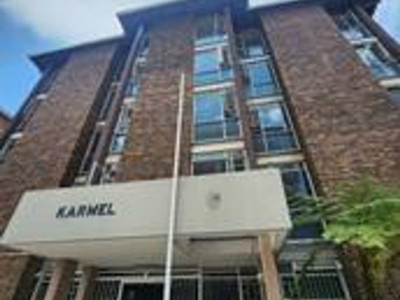 Low angle view of the brick facade and entrance of the Karnel apartment building, featuring security gates and multi-story window arrangements.