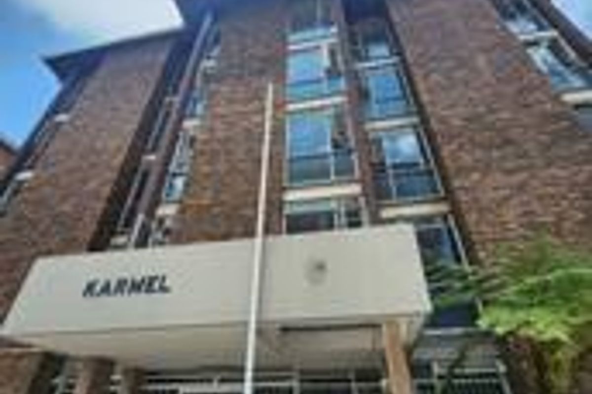 Low angle view of the brick facade and entrance of the Karnel apartment building, featuring security gates and multi-story window arrangements.