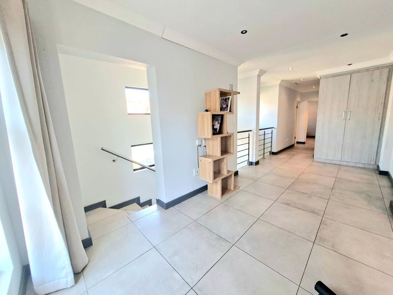 Spacious upper-level landing area featuring large format floor tiles, a staircase with a modern stainless steel handrail, and integrated built-in storage cupboards.