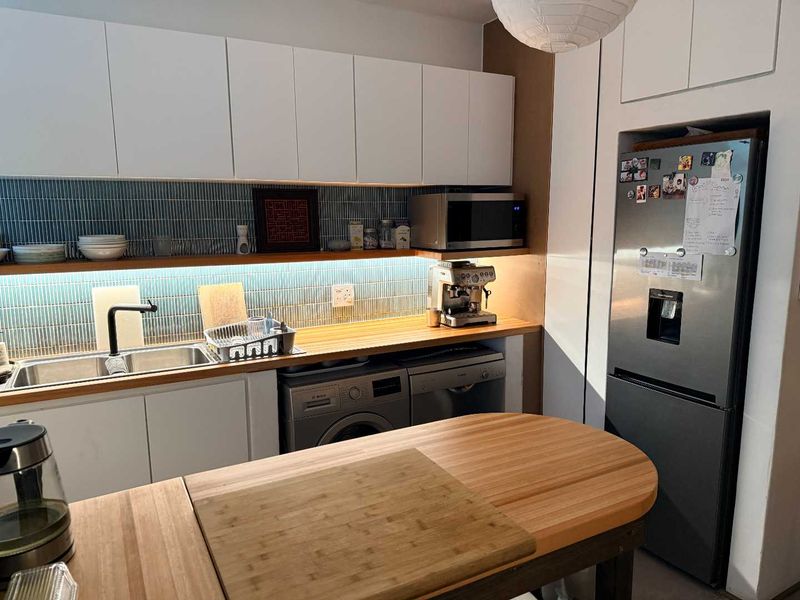 Modern kitchen featuring white cabinetry, wooden countertops, a stylish tiled backsplash, and integrated appliances including a washing machine and dishwasher.