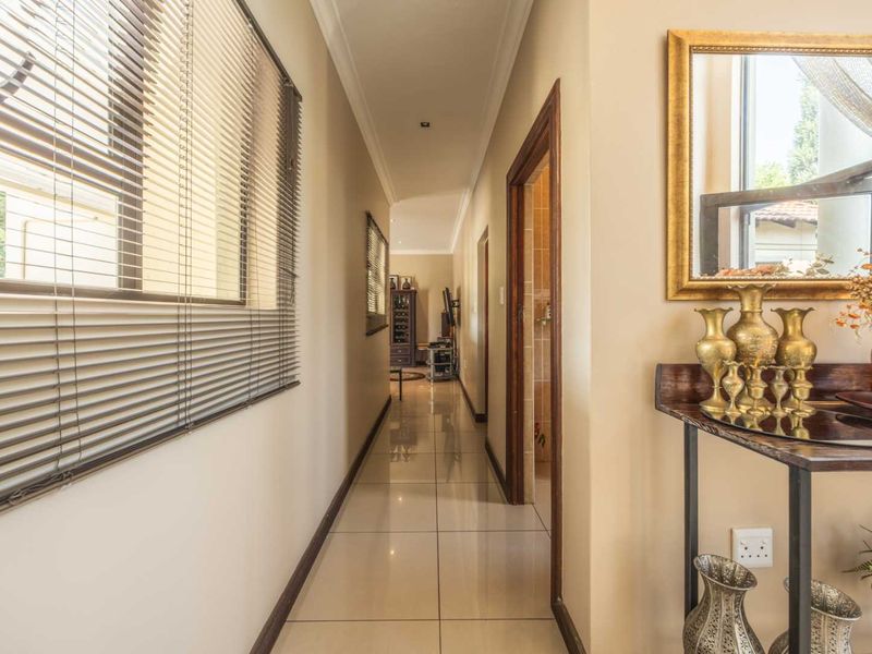 A well-lit hallway featuring neutral tiled flooring, clean wall finishes, and large windows with venetian blinds, providing access to adjacent rooms.
