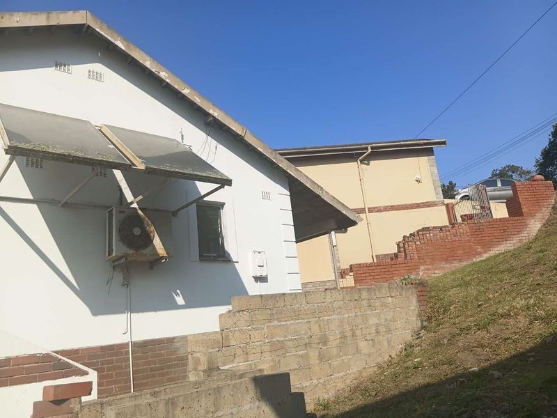 Rear exterior view of the property showing a solar water heater, air conditioning unit, and tiered brick and concrete block retaining walls.