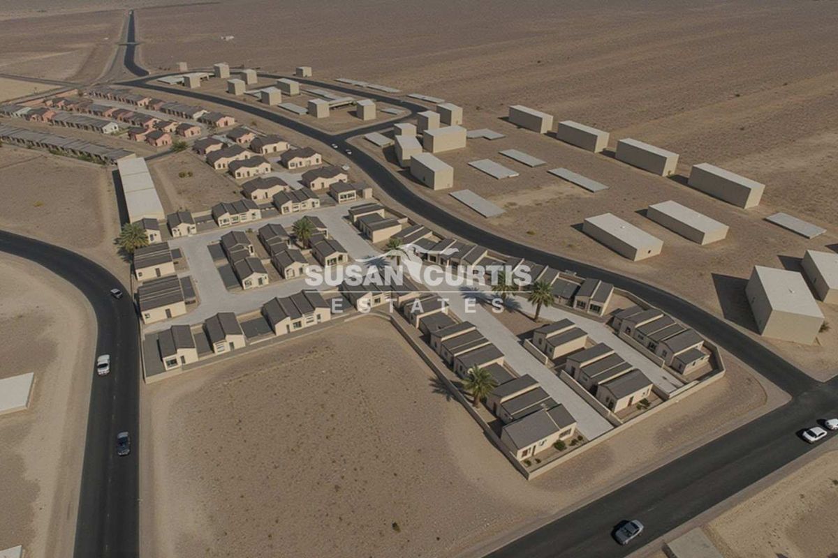 Aerial view of a residential apartment complex development featuring multiple housing units, paved internal roads, and surrounding desert landscape.