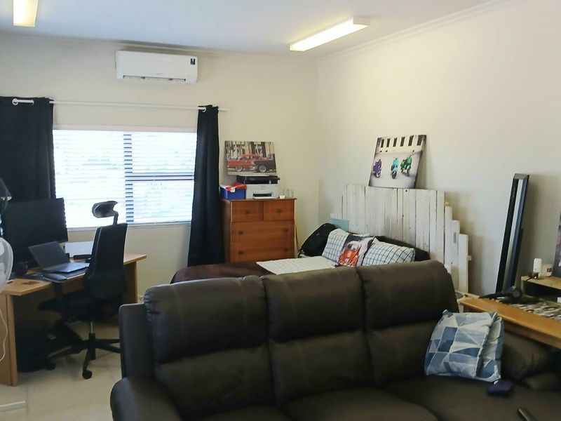 A multi-functional bedroom space featuring a wall-mounted split-system air conditioner, neutral walls, and window blinds.