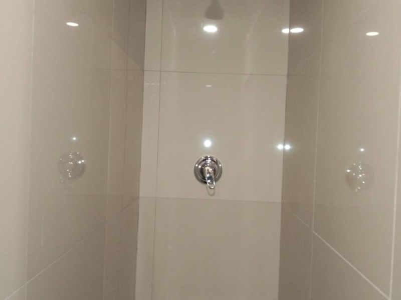 A clean, modern shower enclosure featuring neutral large-format wall tiles and a chrome shower mixer.