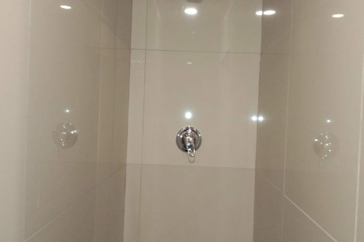 A clean, modern shower enclosure featuring neutral large-format wall tiles and a chrome shower mixer.