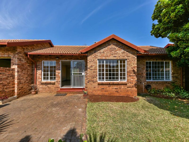 Rear view of a face brick townhouse featuring a paved patio area, garden space, and secure sliding door access.
