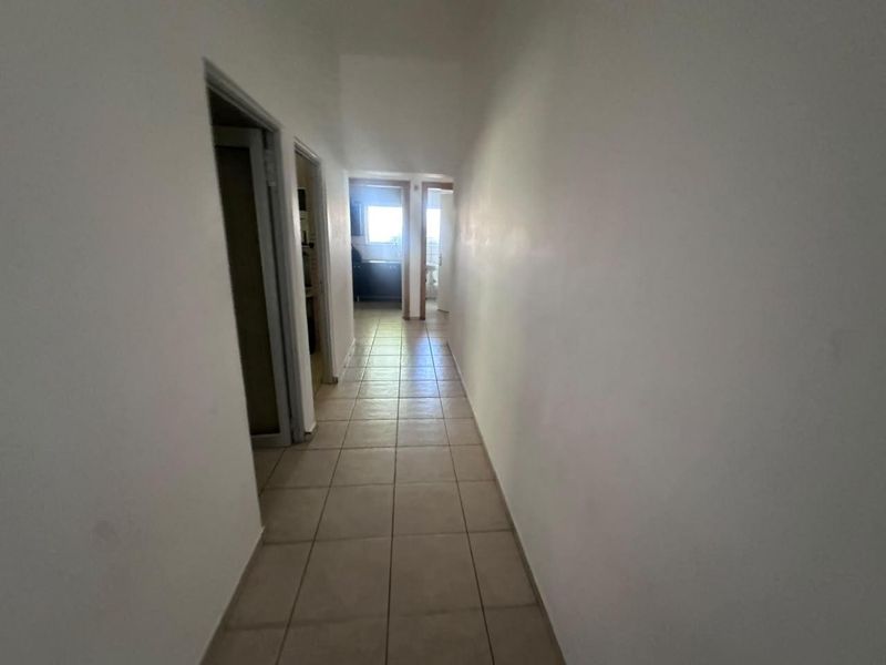 A simple, empty hallway with tiled flooring providing access to multiple rooms within the office space.