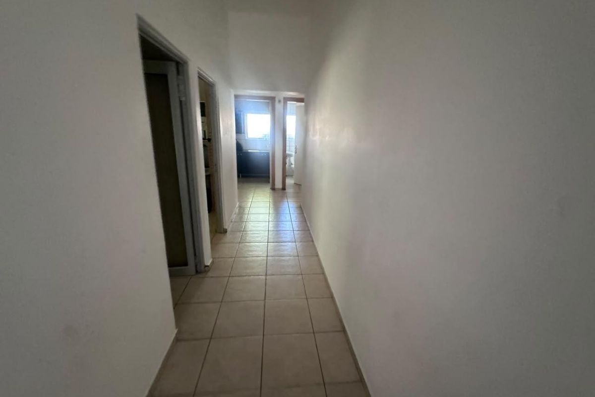 A simple, empty hallway with tiled flooring providing access to multiple rooms within the office space.