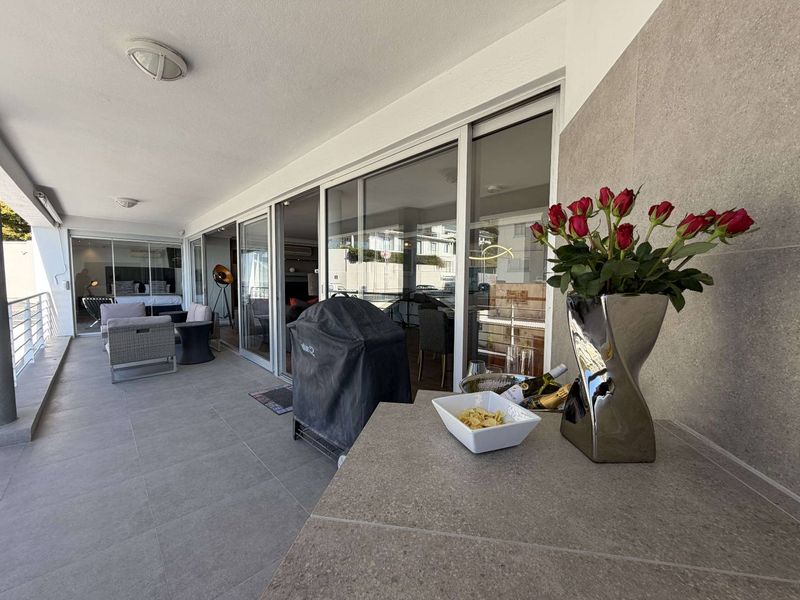 Spacious covered balcony featuring large format floor tiles, stone wall cladding, and expansive sliding glass doors providing seamless indoor-outdoor flow.