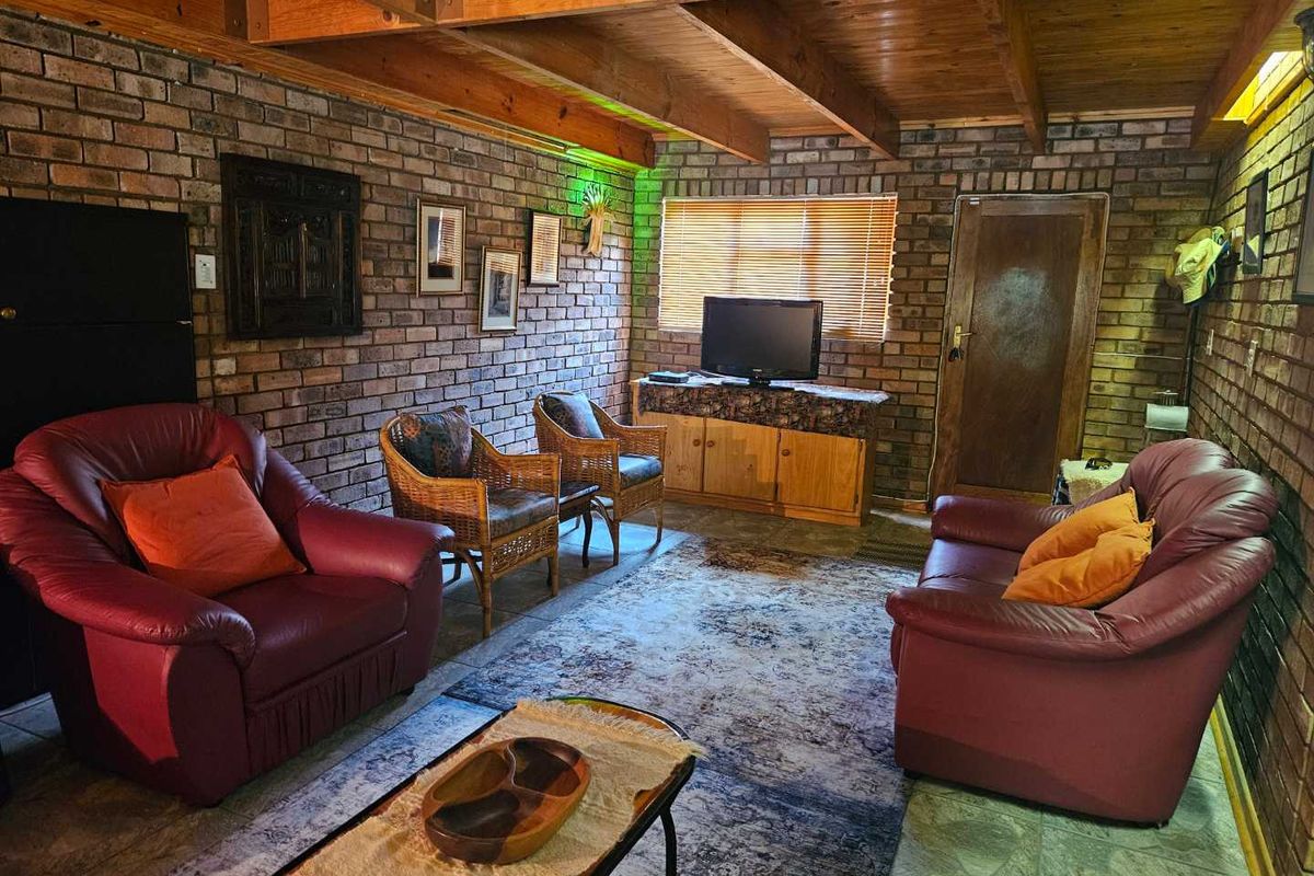 A rustic living room featuring exposed timber ceiling beams, face-brick walls, and tiled flooring, creating a warm and traditional atmosphere.