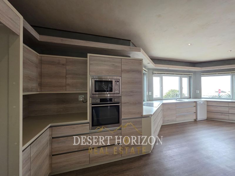Modern kitchen featuring light wood-grain cabinetry, built-in oven and microwave, integrated dishwasher, and ample counter space with large windows.