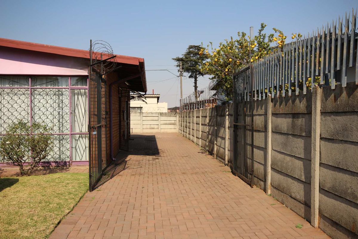 A side access path featuring paved driveway, secure metal gates, and high precast concrete boundary walls topped with security spikes and razor wire.