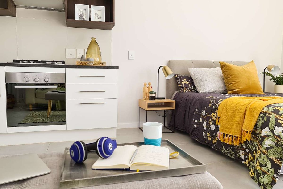A modern open-plan studio apartment featuring a compact kitchen with built-in appliances and a comfortable sleeping area with neutral finishes.
