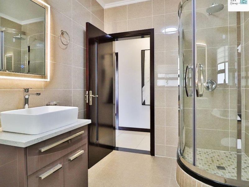 Modern bathroom featuring a sleek vanity with vessel sink, backlit mirror, and a curved glass shower enclosure with tiled finishes.