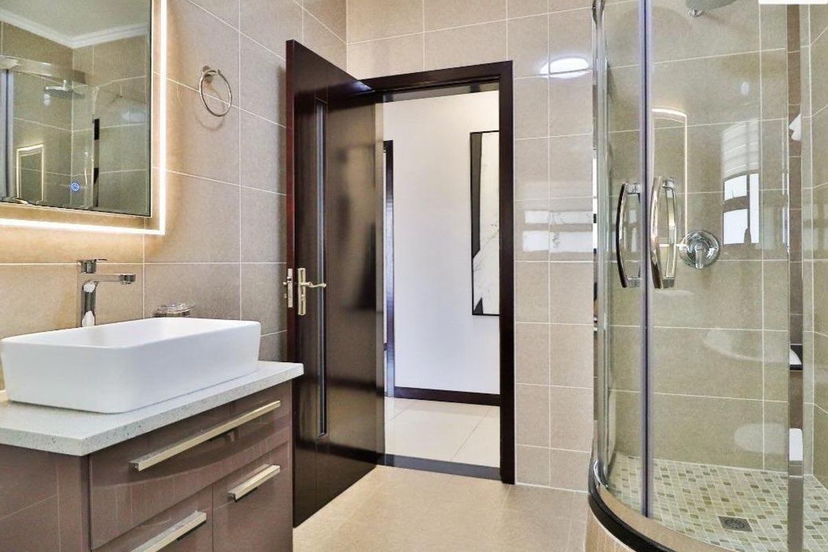 Modern bathroom featuring a sleek vanity with vessel sink, backlit mirror, and a curved glass shower enclosure with tiled finishes.