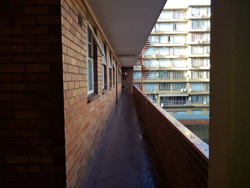 An exterior walkway or balcony featuring brick walls and tiled flooring, providing access to the apartment units.