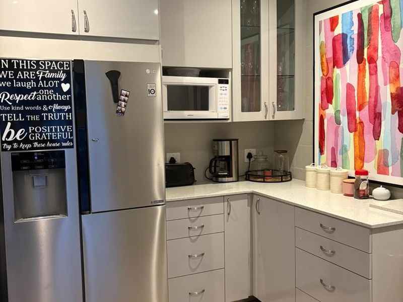 A modern kitchen area featuring light grey cabinetry, stone countertops, and a built-in microwave, providing a clean and functional workspace.