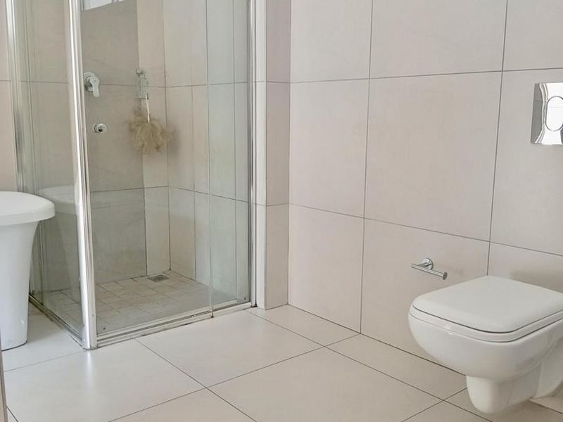 A modern, minimalist bathroom featuring a glass shower enclosure, wall-mounted toilet with a concealed cistern, and neutral ceramic tiling throughout.